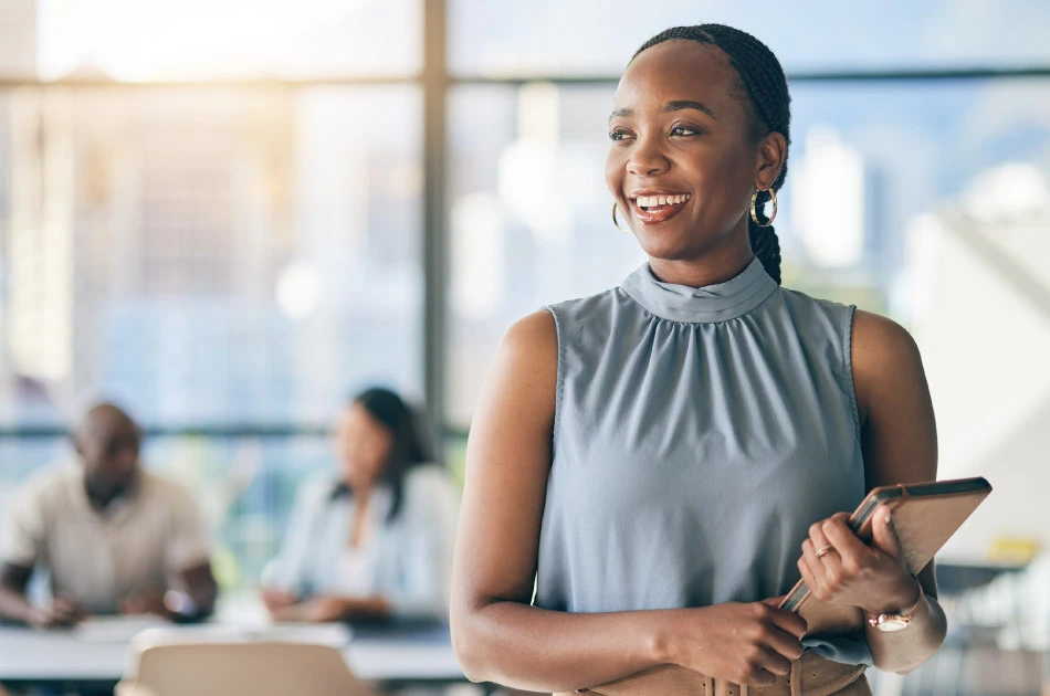 Black woman in office leadership meeting smiling and holding tablet Black woman in office leadership meeting smiling and holding tablet